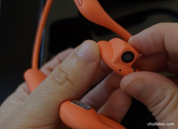 Auriculares de conducción ósea naranjas con cámara integrada, sostenidos entre las manos