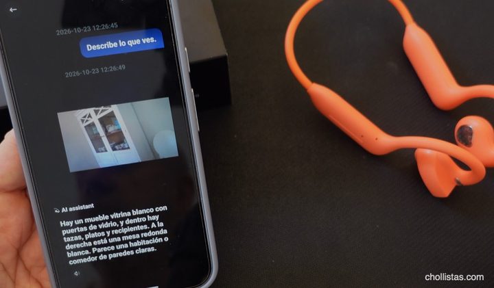 Auriculares de conducción ósea naranjas junto a un móvil donde el asistente de IA describe una habitación